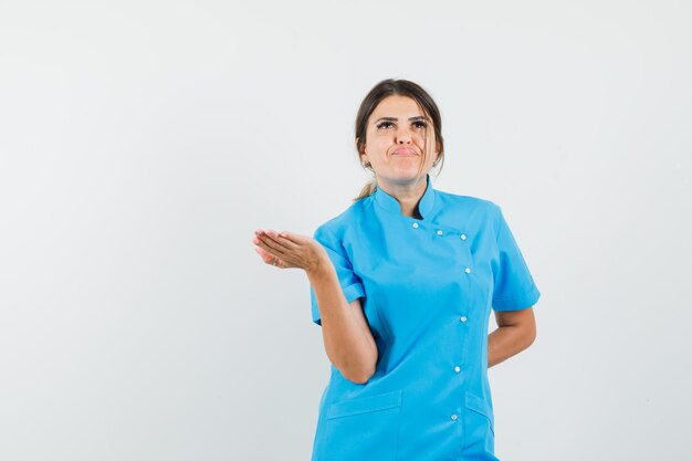 Female doctor raising hand in questioning manner in blue uniform and looking annoyed