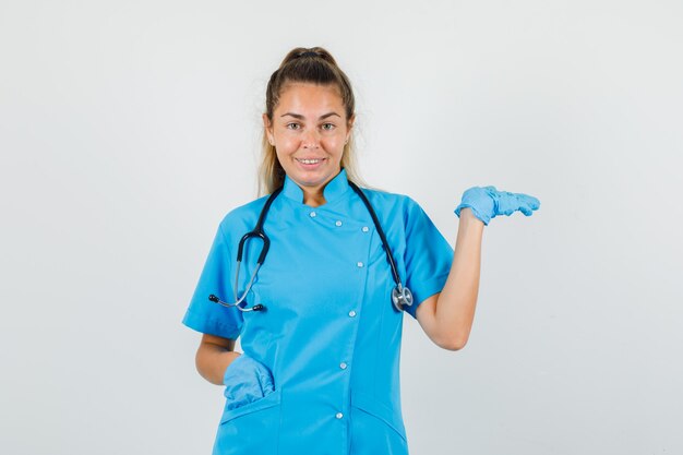 Female doctor raising palm as catching something in blue uniform