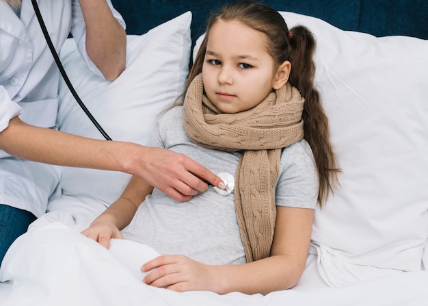 Female doctor's hand examining girl lying on bed with stethoscope