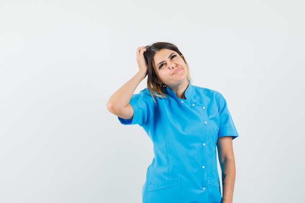Female doctor scratching head while looking up in blue uniform and looking thoughtful