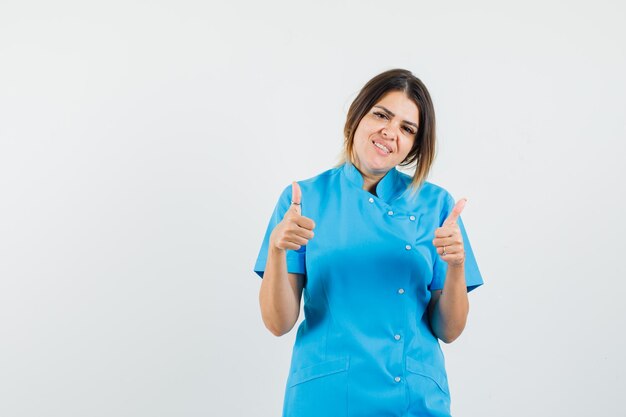 파란색 유니폼에 두 엄지 손가락을 보여주는 여성 의사와 쾌활한 찾고