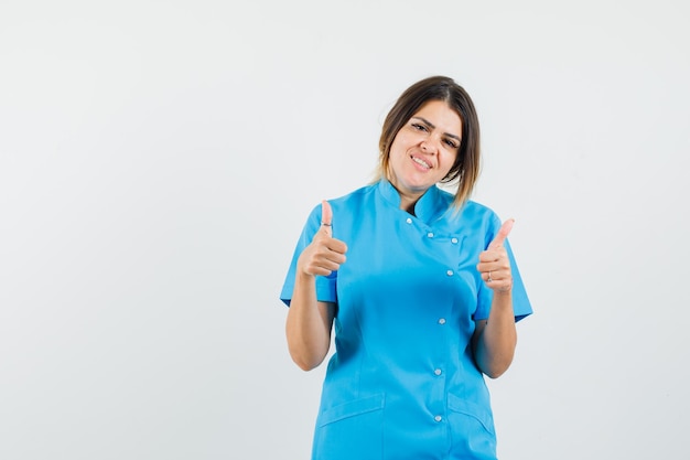 Женщина-врач показывает двойные пальцы вверх в синей форме и выглядит весело