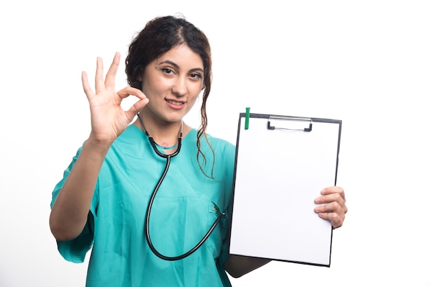 Женский доктор показывая пустой буфер обмена с одобренным жестом на белой предпосылке. Фото высокого качества