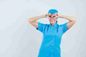 Foto gratuita medico femminile che mostra il gesto del cuore in uniforme blu e che sembra felice, vista frontale.