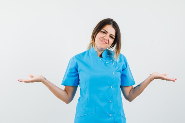 Женщина-врач показывает беспомощный жест в синей форме и выглядит позитивно