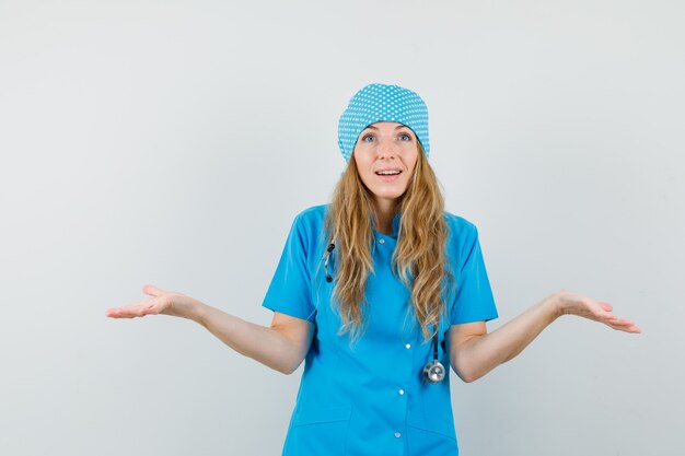 Female doctor showing helpless gesture in blue uniform and looking puzzled. 