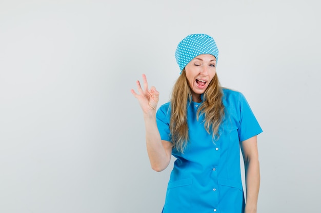 Free photo female doctor showing ok gesture and winking eye in blue uniform