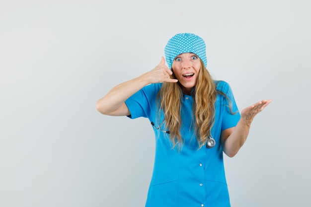 Женщина-врач показывает жест телефона в синей форме и выглядит полезной