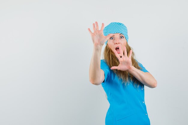 Female doctor showing refusal gesture in blue uniform and looking scared. 