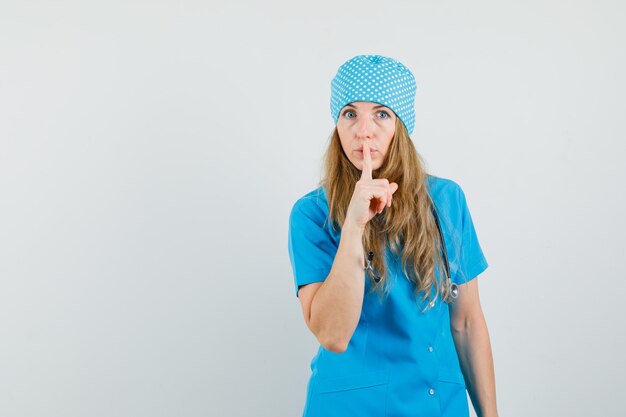 Female doctor showing silence gesture in blue uniform and looking careful 