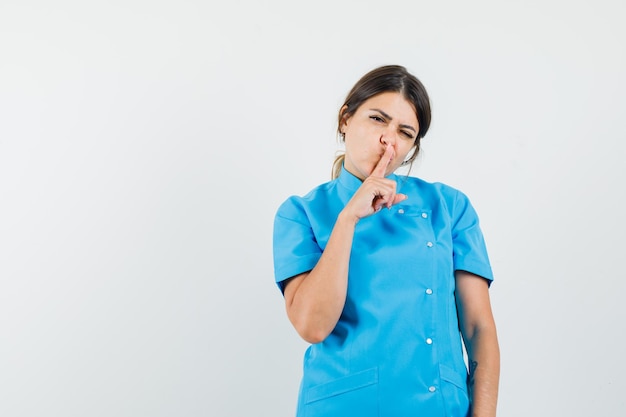 Female doctor showing silence gesture in blue uniform and looking careful