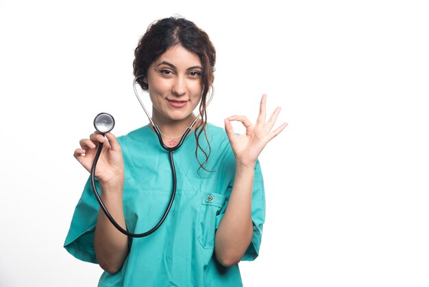 Female doctor showing stethoscope with ok gesture on white background