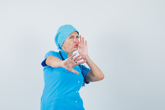 Free photo female doctor showing stop gesture with mouth shut as zip in blue uniform and looking scared , front view.