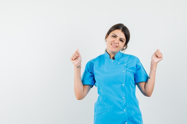 Женщина-врач показывает жест успеха в синей форме и выглядит удачливой
