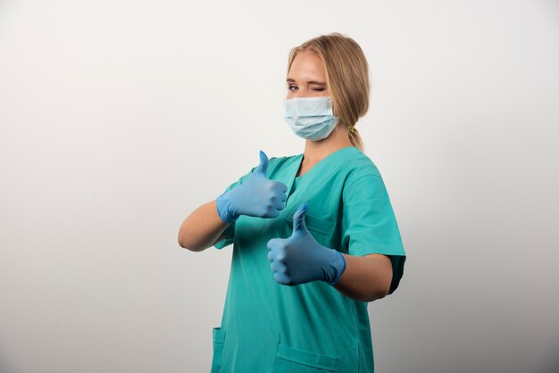 Female doctor showing thumb up and wearing a medical mask. 