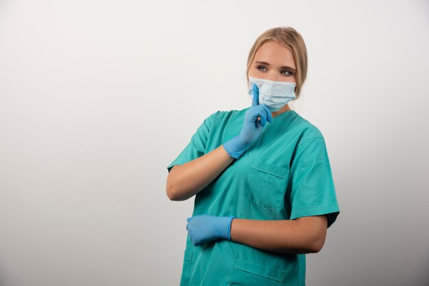 여성 의사가 엄지손가락을 치켜들고 의료용 마스크를 쓰고 있습니다.