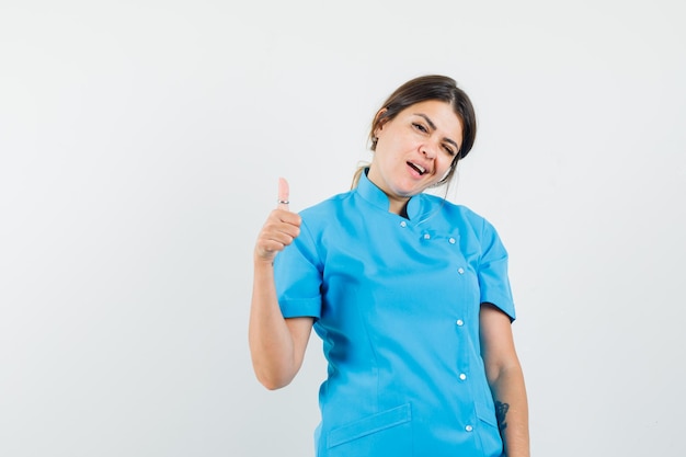 Female doctor showing thumb up, winking eye in blue uniform