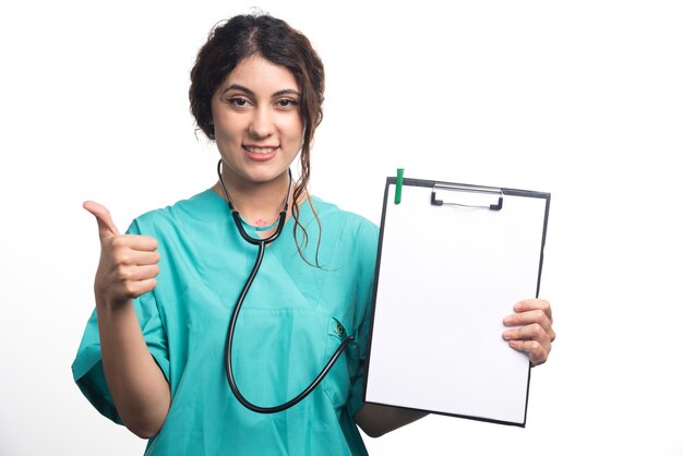 白い背景の上の空のクリップボードで親指を示す女性医師。高品質の写真