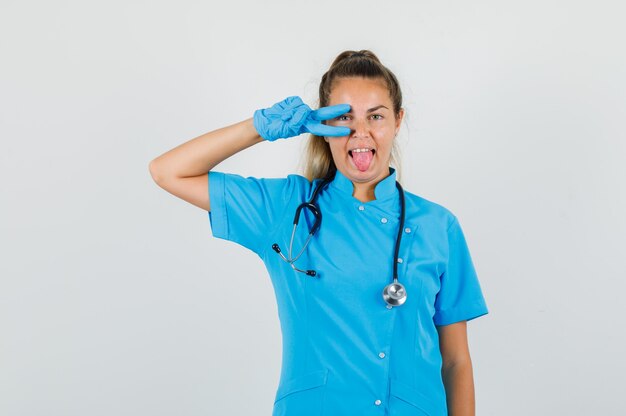 Female doctor showing v-sign on eye in blue uniform