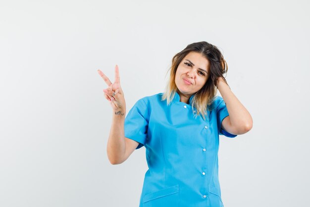 Female doctor showing victory sign in blue uniform and looking sharming