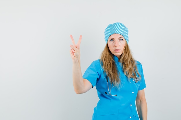 青い制服を着た勝利のサインを示す女性医師