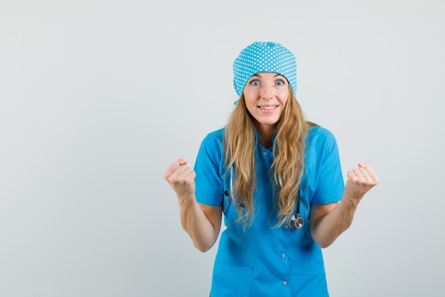 파란색 유니폼과 행복을 찾고 승자 제스처를 보여주는 여성 의사.