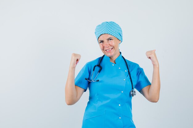파란색 유니폼에 승자 제스처를 보여주는 여성 의사와 행운, 전면보기를 찾고.