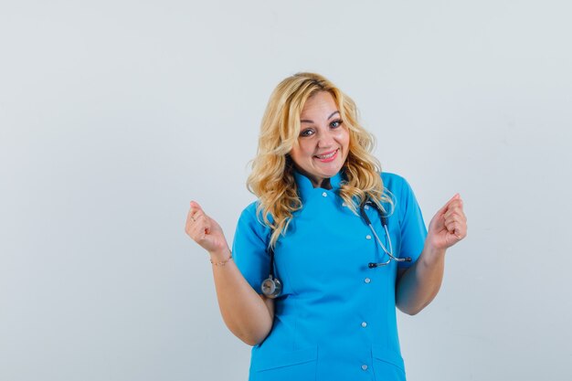 Female doctor showing winner gesture in blue uniform and looking pleased.