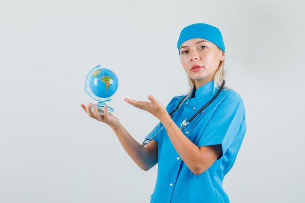 Female doctor showing world globe in blue uniform and looking careful.