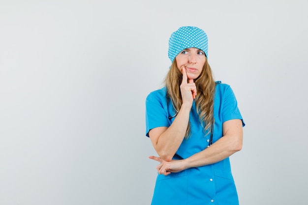 Foto gratuita medico femminile che sta nella posa di pensiero in uniforme blu e che sembra esitante.