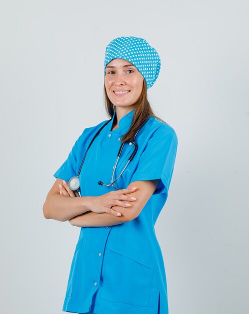 파란색 유니폼에 교차 팔으로 서 기쁜 찾고 여성 의사. 전면보기.