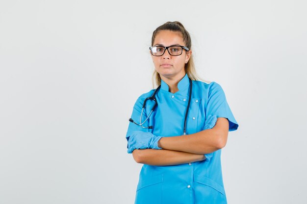 파란색 유니폼에 교차 팔으로 서 여성 의사