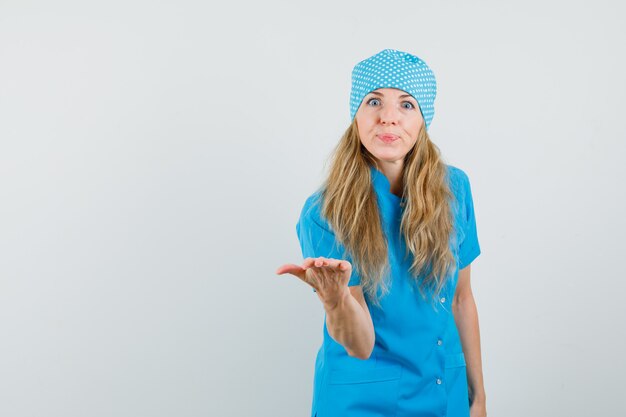 Женщина-врач протягивает руку в вопросительном жесте в синей форме