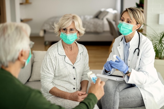 Female doctor talking to senior couple while vising them at home during coronavirus quarantine