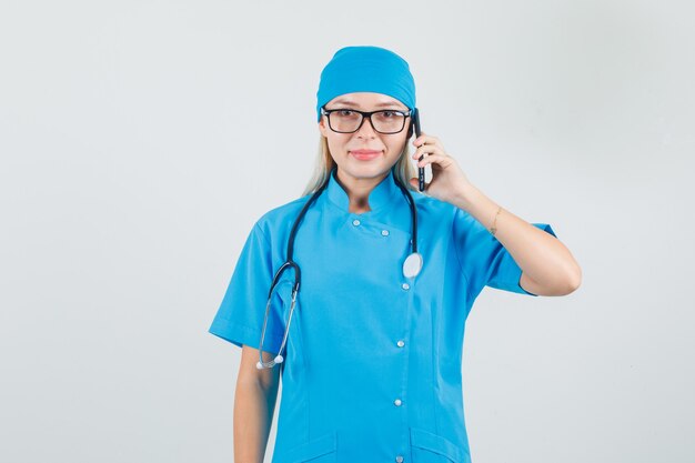 スマートフォンで話し、青い制服を着て笑っている女性医師