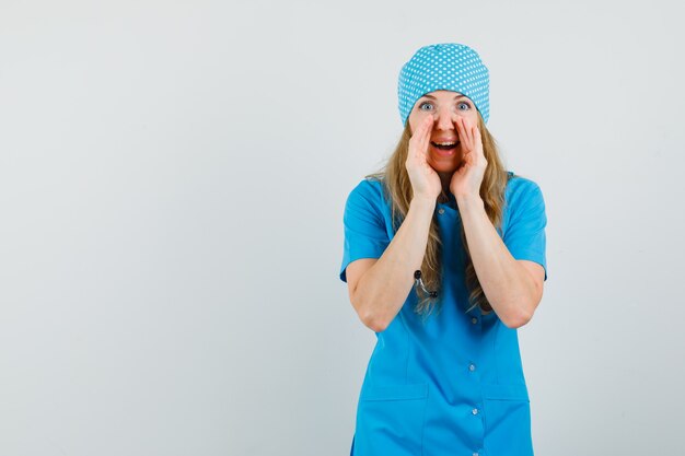 Female doctor telling secret with hands near mouth in blue uniform and looking curious 