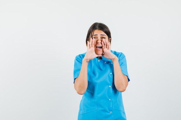 Female doctor telling secret with hands near mouth in blue uniform