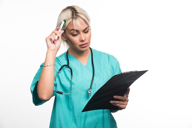 Female doctor thinking about something while holding clipboard on white surface
