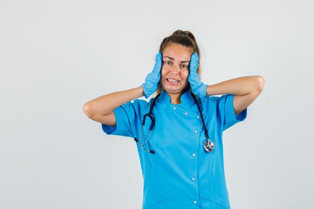 Female doctor touching face with hands in blue uniform