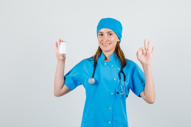 Female doctor in uniform holding bottle of pills with ok sign and looking merry