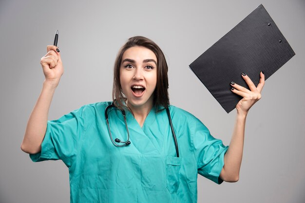 Женщина-врач в униформе смеется, держа в руках буфер обмена. Фото высокого качества