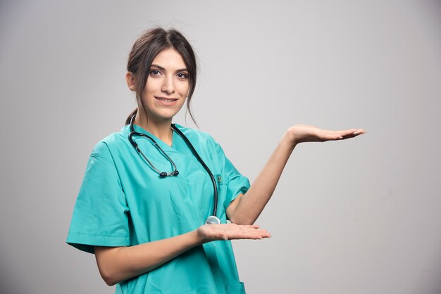 Женщина-врач в униформе позирует на сером