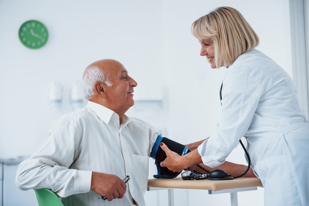 Женщина-врач использует тонометр для измерения артериального давления пожилому мужчине.