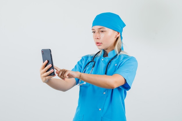 Женщина-врач с помощью смартфона в синей форме и выглядит занятой.