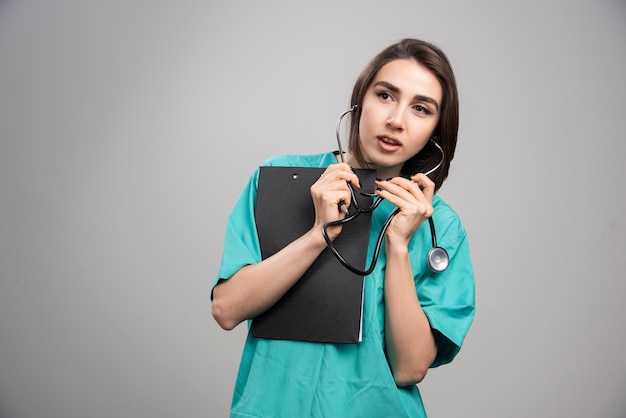 Medico donna utilizzando uno stetoscopio sul muro grigio.