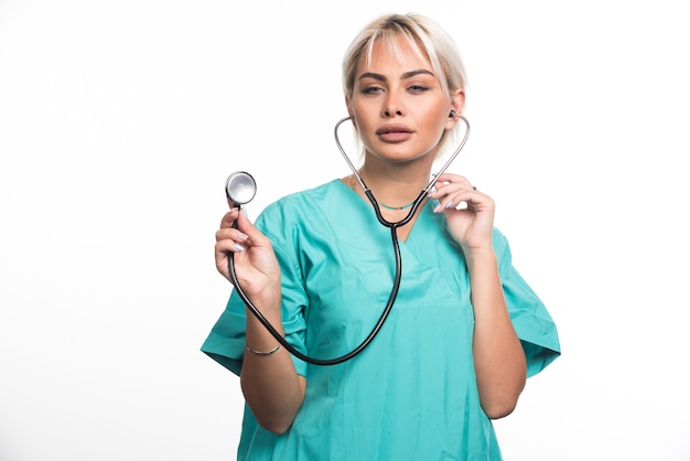 Female doctor using stethoscope on white wall .