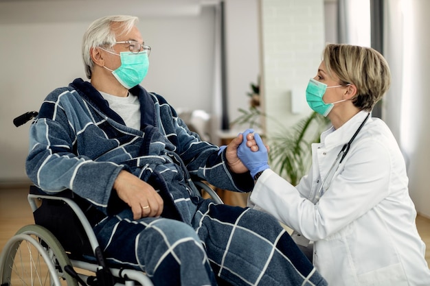 Female doctor visiting disabled mature man at home during coronavirus pandemic