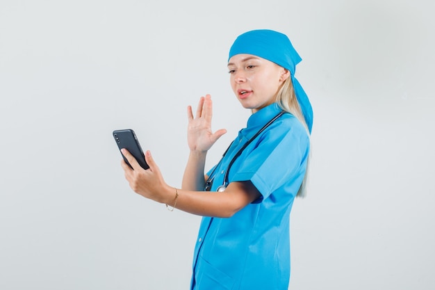 青い制服を着てビデオ通話に手を振って、ポジティブに見える女性医師