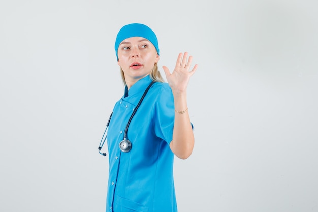 Женщина-врач, махнув рукой, оглядываясь назад в синей форме.