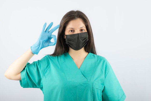 Женщина-врач в черной медицинской маске и показывая жест ОК.